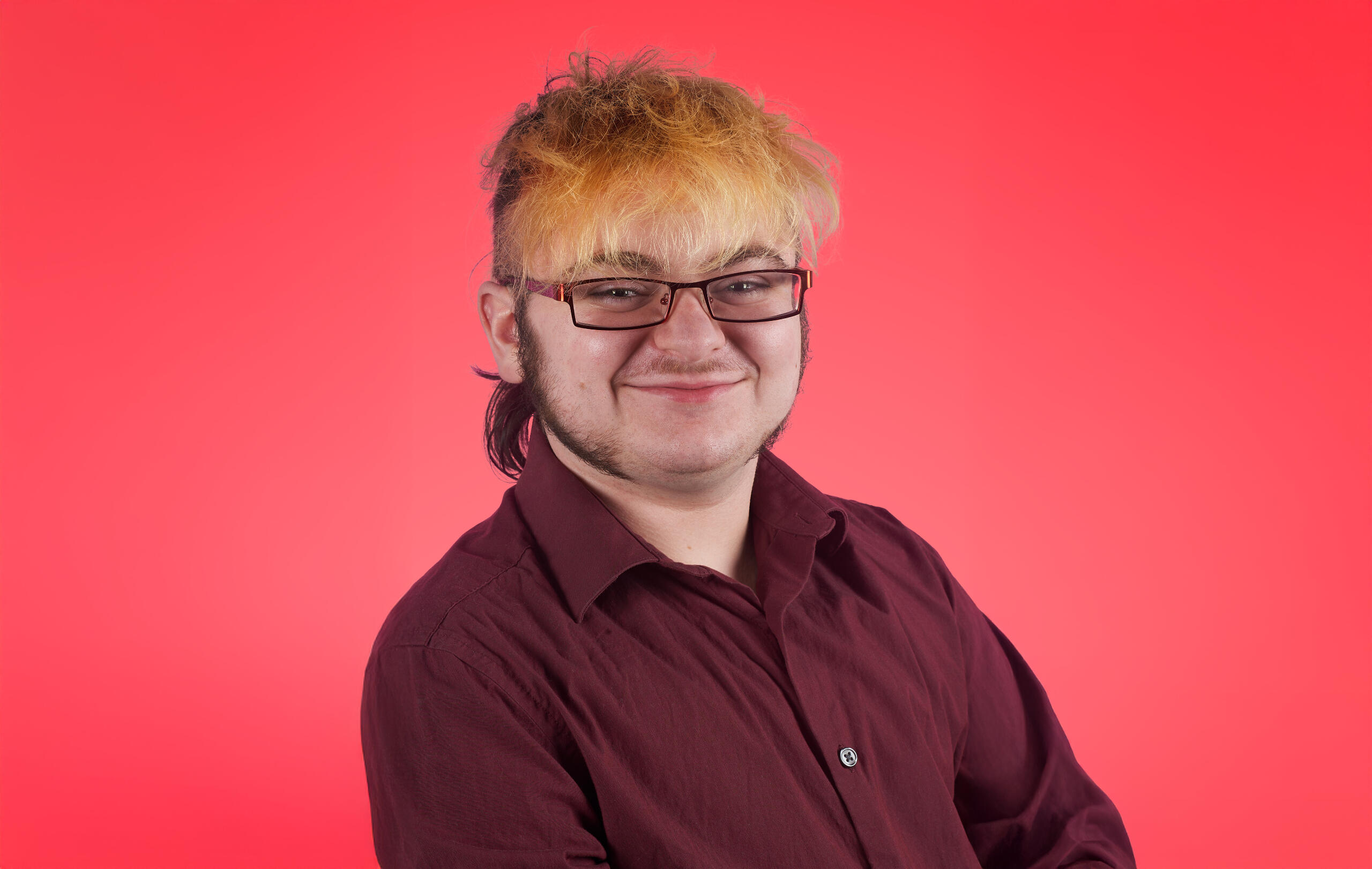 Headshot of Lyle O. Lewis wearing a maroon button down on a vibrant red bacground.