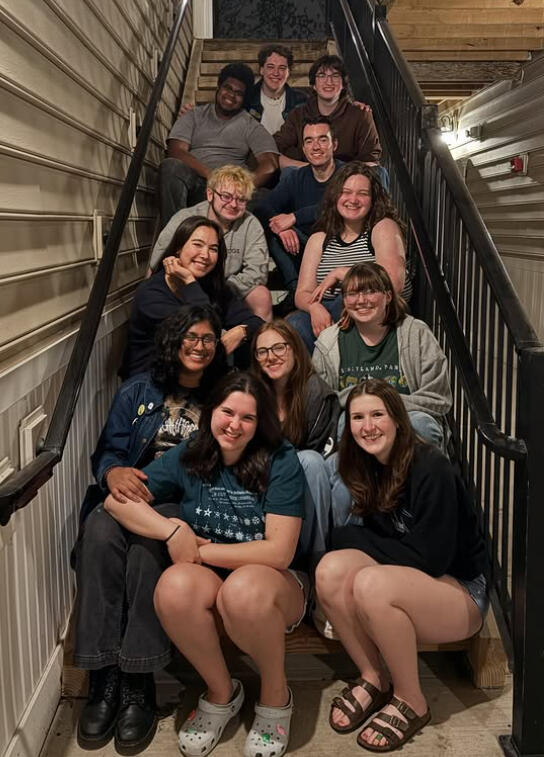 A large group of people are sitting on the steps of an apartment complex so everyone is in the frame
