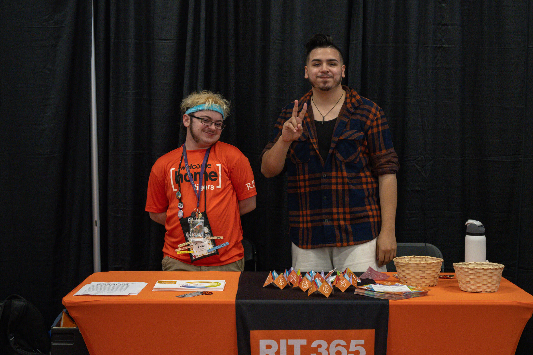 Lyle and second peer facilitator are standing at a table with an orange RIT 365 banner over it, posing for the picture