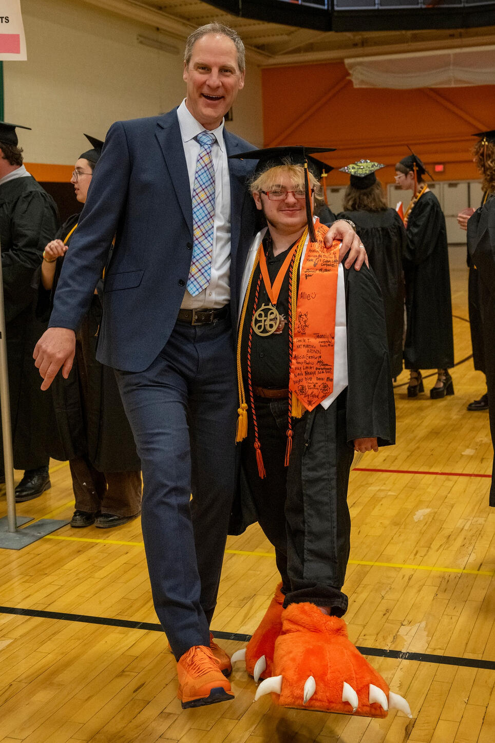Lyle and Todd are standing next to each other showing off their tiger feet and orange shoes respectively, Todd is significantly taller than Lyle