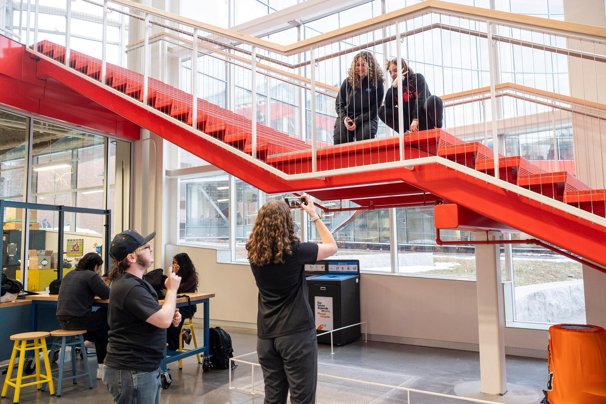two students crouch on a staircase while lyle and another student look from below, lyle is directing the one student on how to frame the photo