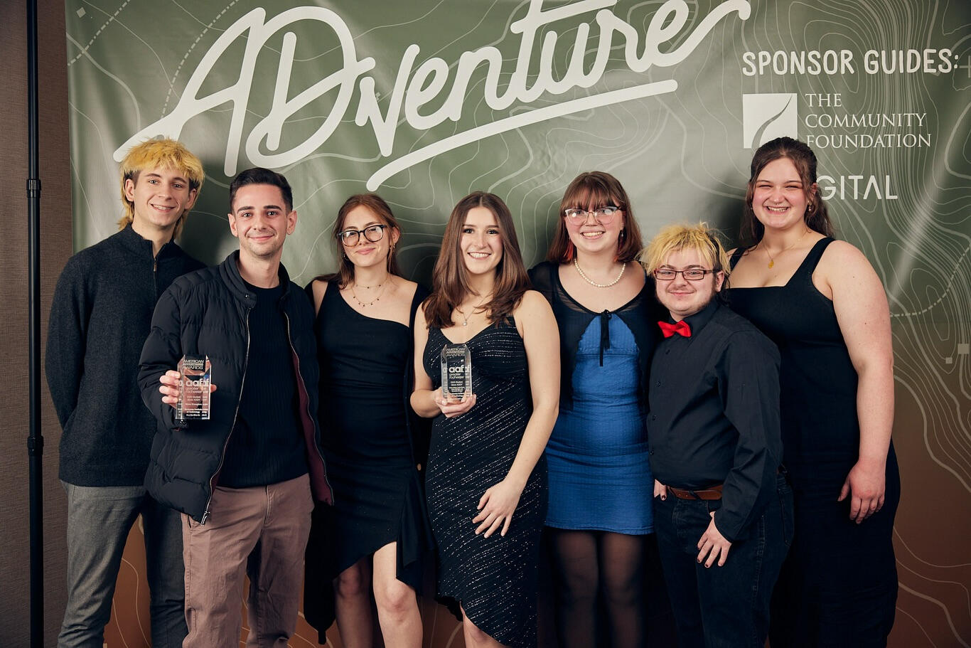 Seven designers, including Lyle, standing in front of a backdrop reading AD-venture, two of the designers are holding awards they won at the ceremony.