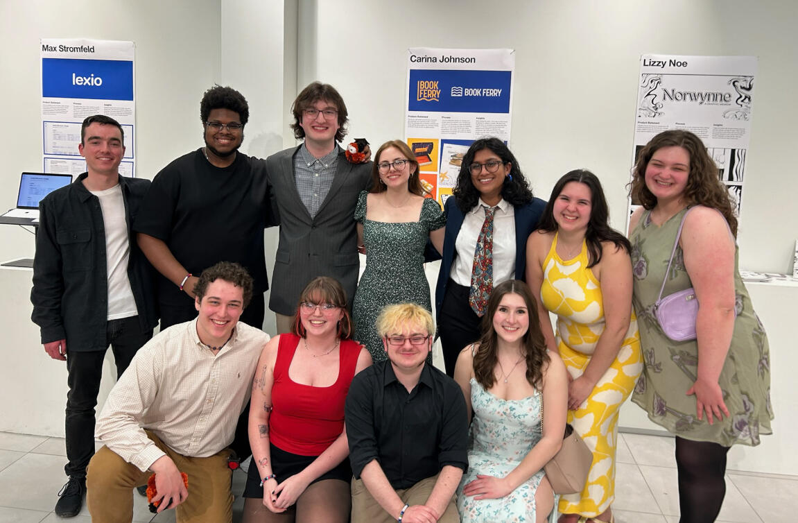 a group of people stand in two rows in front of their friends' projects that are being displayed in a professional gallery