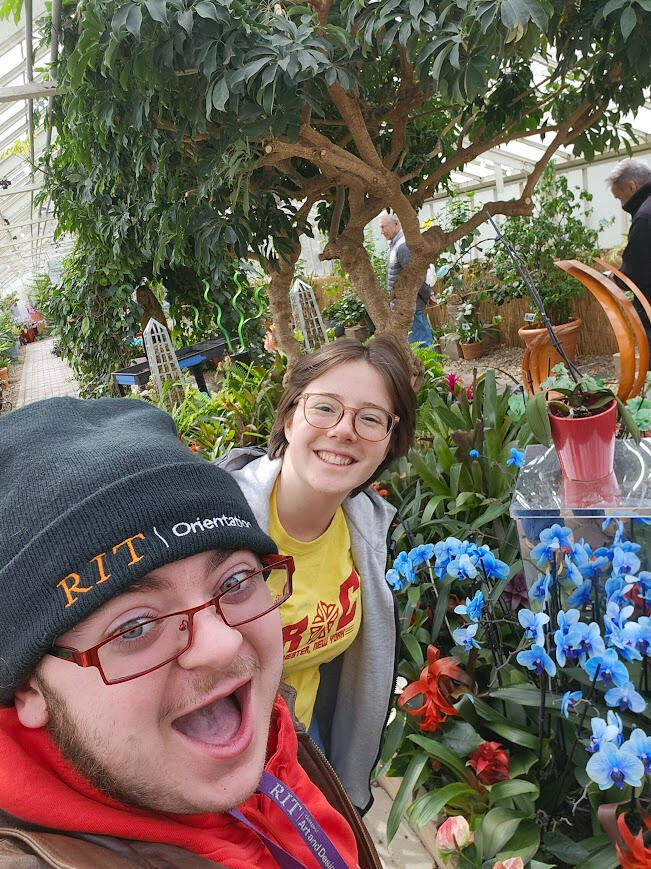Lyle O. Lewis taking a selfie in front of beautiful flowers with his friend Penelope standing behind him