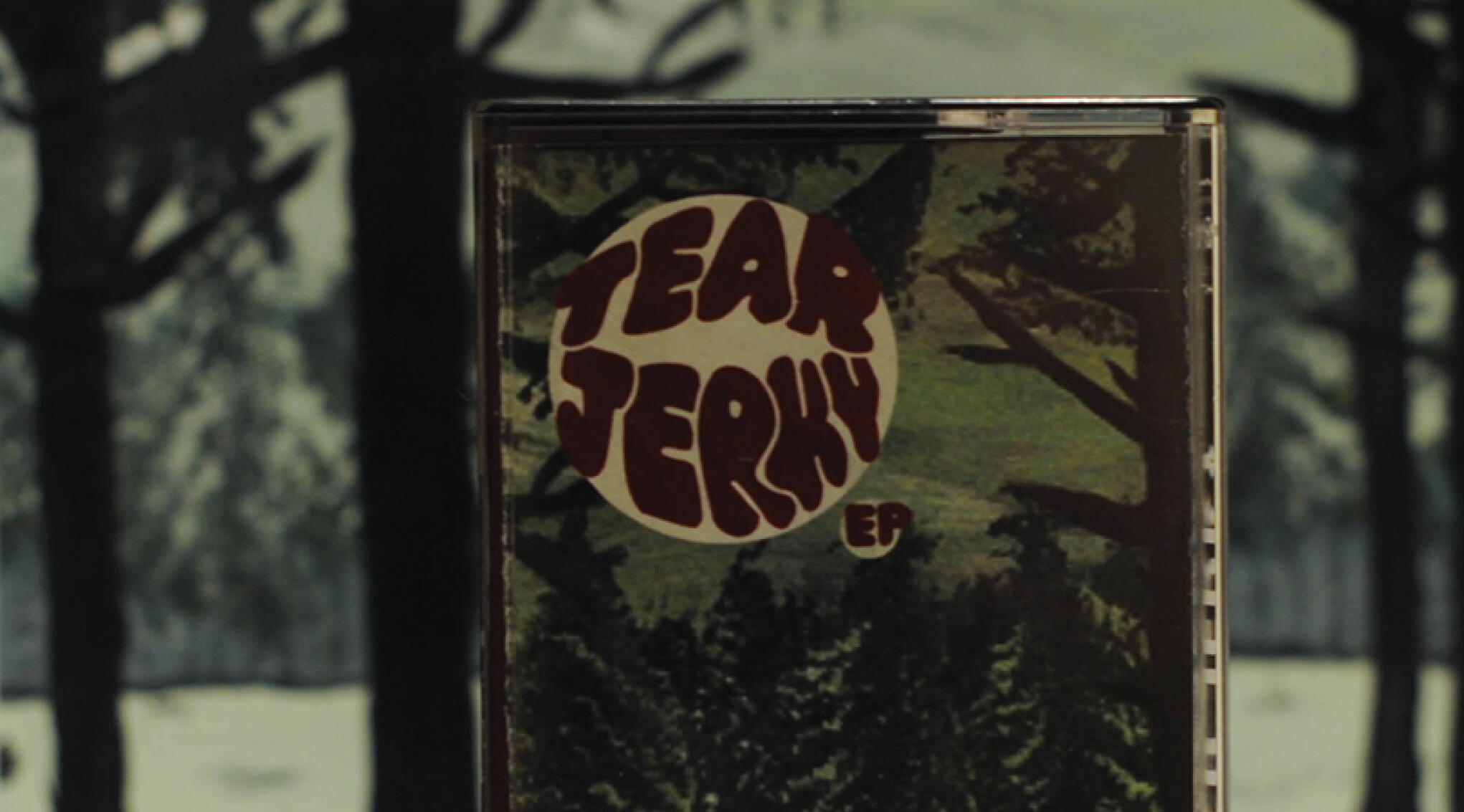 Image of a cassette case with a painting of a snowy forest and hand letter logo that stats "tear jerky, EP"